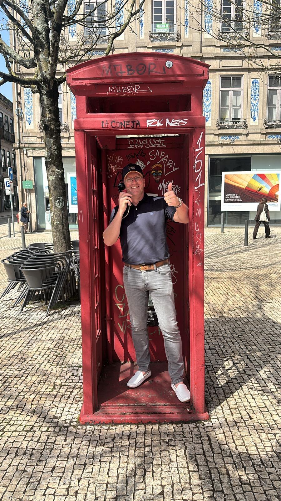 Joost van Beers in een rode telefooncel, duim omhoog